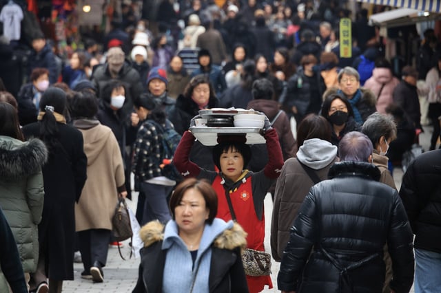 A woman carrying meals on her head makes her way through shoppers at a traditional market in Seoul, South Korea, January 4, 2024.   REUTERS/Kim Hong-Ji