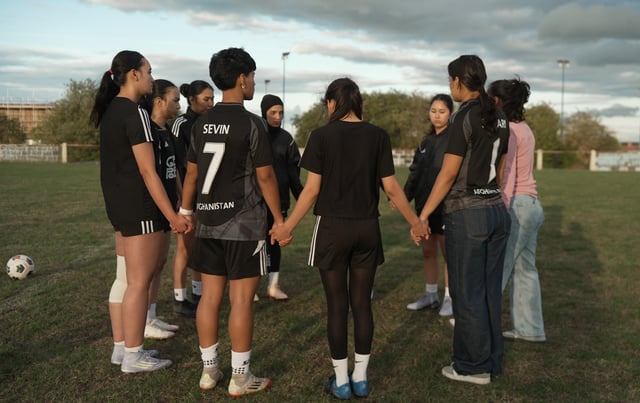 Afghan women soccer players hold hands before a training session.