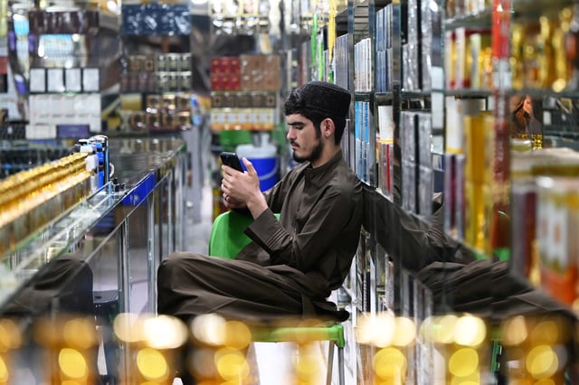 An Afghan vendor selling perfume and body sprays, uses his mobile phone as he sits at his shop in Kabul on October 1, 2025.