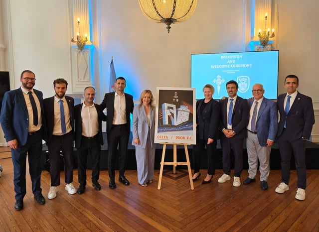 Directivas del Celta y el PAOK posan con el cartel conmemorativo del partido