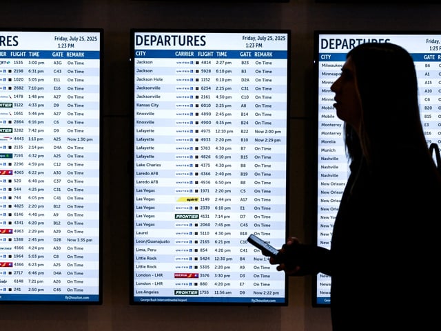 A woman walks past various screens displaying flight information at George Bush Intercontinental Airport on July 25, 2025, in Houston, Texas. (Photo by RONALDO SCHEMIDT / AFP)