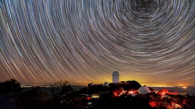 DESI maps distant objects to study dark energy. The instrument is installed on the Mayall Telescope, shown here beneath star trails.