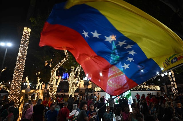 Una mujer ondea una bandera venezolana mientras la gente pasa junto a una decoración navideña en la Plaza Bolívar de Caracas, el 1 de octubre de 2025