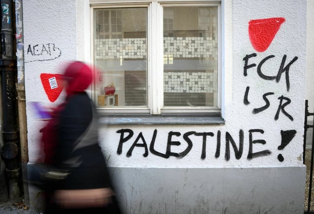 Eine Person geht an einer mit Graffity besprühten Hauswand vobei. Dort steht FCK ISR Palestine!
