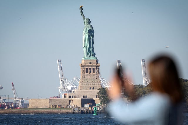 A woman photographs the Statue of Liberty from Battery Park during the first day of a partial U.S. government shutdown in New York City, New York, U.S., October 1, 2025. REUTERS/Brendan McDermid/File Photo