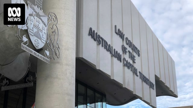 The sign out of the front of the building and the crest, with an autumnal tree nearby and a blue sky beyond.
