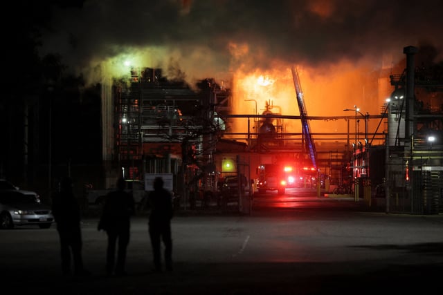 People stand nearby as firefighters work to contain a large fire that broke out at the Chevron refinery in El Segundo, California, on Thursday.