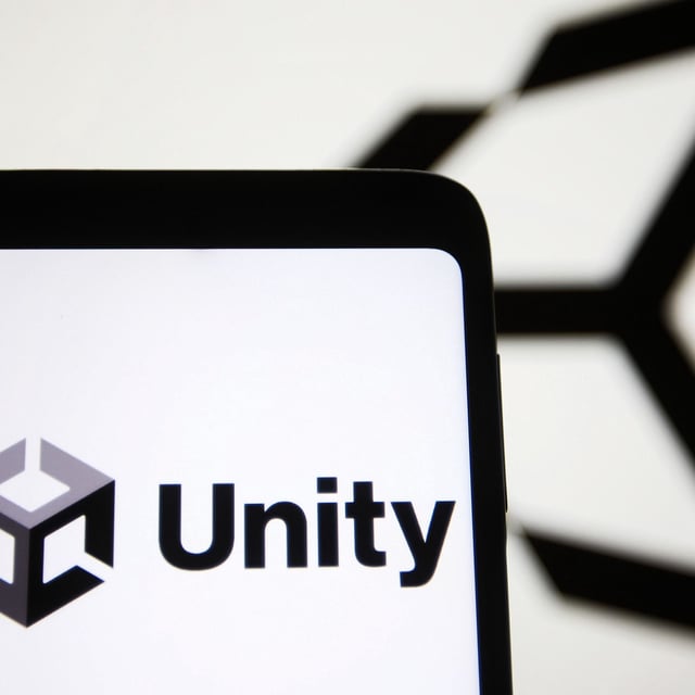 The Unity logo on a phone in front of the Unity logo on a wall.