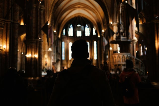 A man walks through a dark church amidst prayer (Photo: Mark Kassinos / Unsplash)