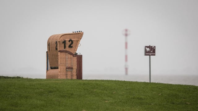 Ein leerer Strandkorb steht unter einem grauen, regnerischen Himmel am Kutterhafen von Wremen