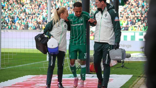 Werders Verteidiger Felix Agu wird nach einer Verletzung am Knöchel von zwei Betreuern vom Spielfeld geführt.