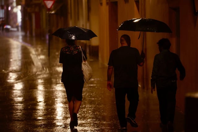 Los transeúntes se protegen de la lluvia este domingo por la noche en València.