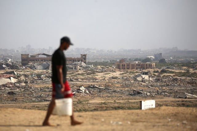 A Palestinian man transports buckets of water next to a coastal path northwest of Nuseirat refugee camp after being displaced southward following an Israeli announcement of closing Al-Rashid road towards the north of the besieged Gaza Strip on Saturday. (Eyad Baba/AFP/Getty Images/TNS)