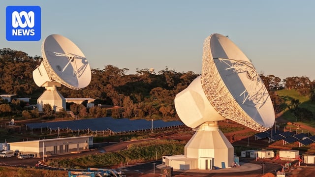 Two large space antennas surrounded by trees and red dirt in New Norcia.