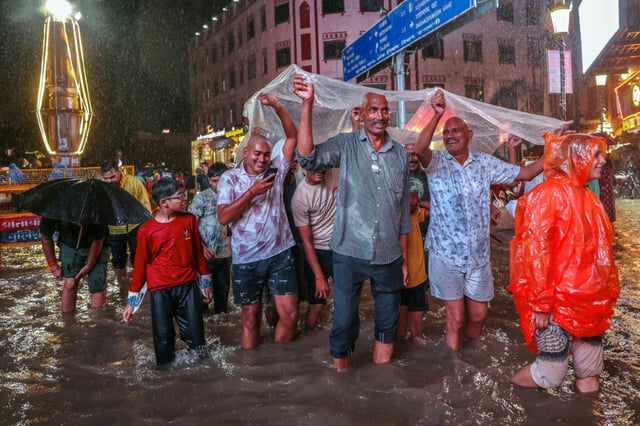 Des habitants s'abritent d'une bâche en plastique dans une rue inondée pendant de fortes pluies de mousson, le 3 octobre 2025 à Varanasi, en Inde
