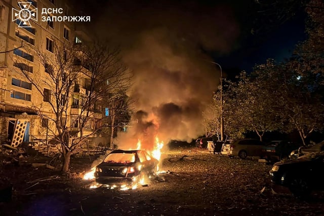 Photo prise et diffusée par les services d'urgence ukrainiens, le 5 octobre 2025, montrant une voiture en feu dans la cour d'un immeuble résidentiel après une attaque aérienne russe à Zaporijjia, en Ukraine