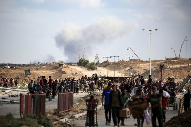 A plume of smoke rises in the background as Palestinians return from a food distribution point run by the US and Israeli-backed Gaza Humanitarian Foundation (GHF) group, near the Netsarim corridor in the central Gaza Strip on October 5, 2025. 
(EYAD BABA/ AFP)