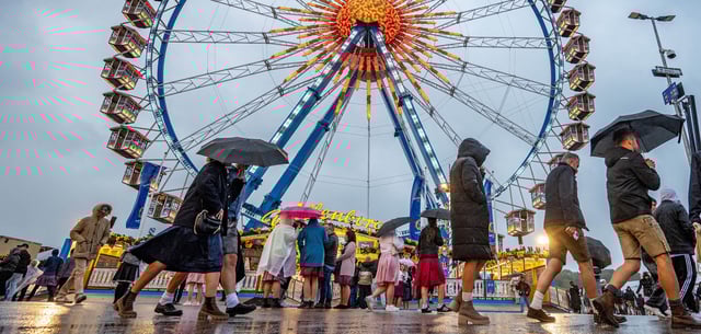Besucher des Oktoberfestes gehen im Regen über das Festgelände