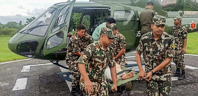 Photo du 5 octobre 2025, prise et diffusée par l'armée népalaise, montrant des militaires transportant une victime évacuée par hélicoptère après des glissements de terrain et des inondations provoqués par de fortes pluies au Népal