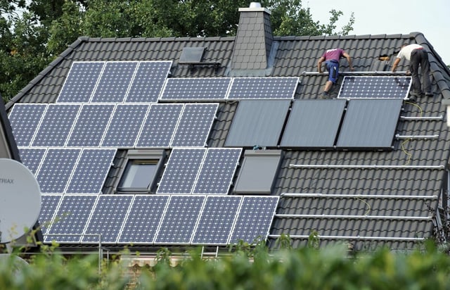 Im brandenburgischen Dallgow-Döberitz installieren zwei Männer auf dem Dach eines Einfamilienhauses eine Solaranlage