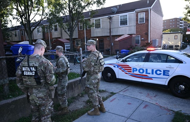 Miembros de la Guardia Nacional se quedan atrás mientras oficiales de policía y agentes policiales federales investigan la escena de un tiroteo en el sureste de Washington, DC, el 2 de octubre de 2025. (Foto de Brendan SMIALOWSKI / AFP)
