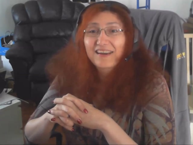 Videogame programmer Rebecca Heineman sitting in home office with clasped hands addressing camera.