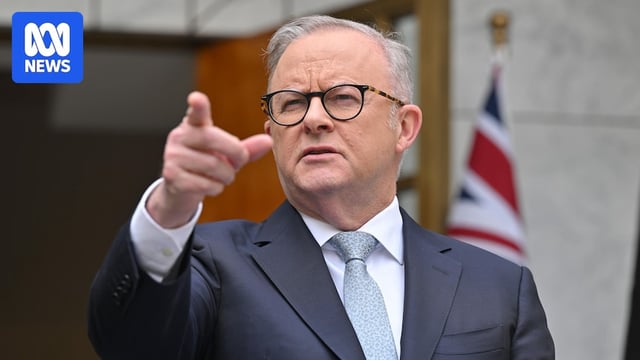 Man in suit points into the distance, stands in front of Australian flag