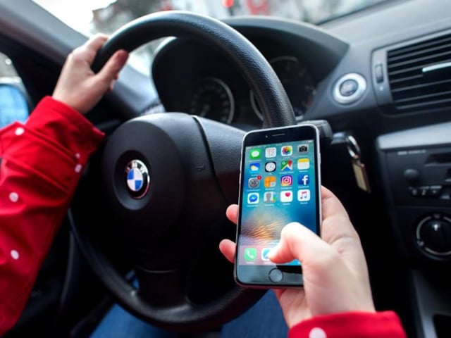 Eine junge Frau sitzt in einem Auto am Steuer und bedient dabei ihr Smartphone.