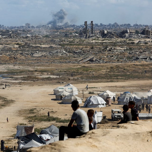 Palestinians look on as smoke rises after explosions in Gaza City on Sunday, as seen from the central Gaza Strip.