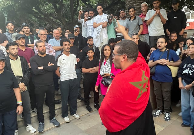A man with a Moroccan flag draped over his shoulders gestures, as demonstrators attend a protest for social justice, near the parliament building, in Rabat, Morocco, October 3, 2025. REUTERS/Ahmed El Jechtimi