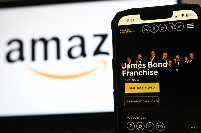 In this photo illustration created in London on February 23, 2025 the MGM Studios website displays James Bond Franchise details on a phone screen next to an Amazon logo displayed on a laptop screen.