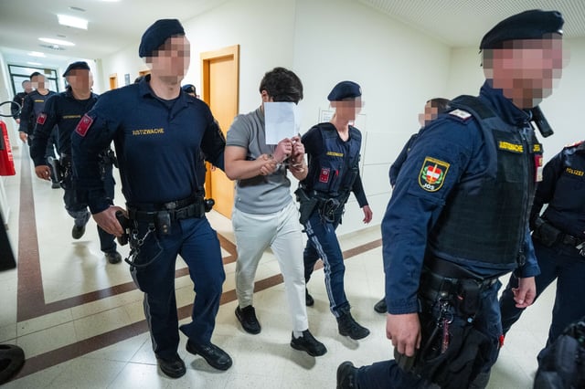 Einer der angeklagten Jugendlichen wird von Polizisten in den Gerichtssaal geführt. Er trägt Handschellen.