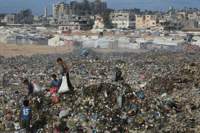 Des enfants palestiniens cherchent des objets à sauver dans un tas d'ordures près de destructions dans le camp de réfugiés de Bureij, dans le centre de la bande de Gaza, le 6 octobre 2025