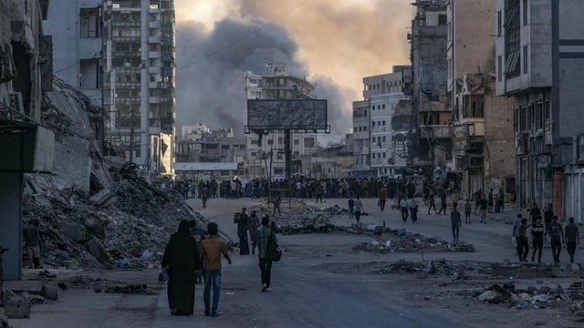Palestinos se desplazan mientras se eleva el humo tras el ataque aéreo israelí en el barrio de Tal Al Hawa durante una operación militar israelí en la ciudad de Gaza.