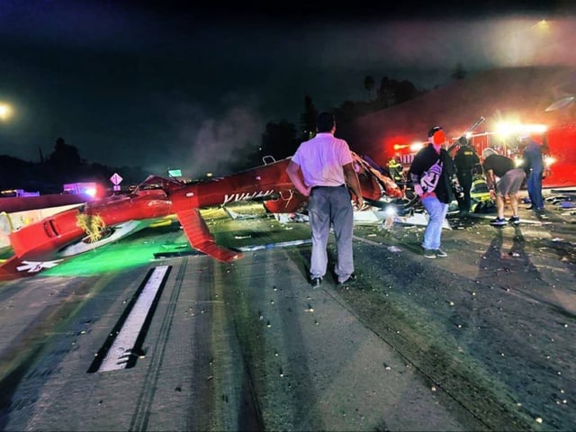 Helicóptero médico rojo siniestrado en plena autopista en Sacramento, rodeado de escombros y personal de emergencia atendiendo la escena bajo luces nocturnas, con ambulancias, camiones de bomberos y civiles observando la situación tras el accidente.