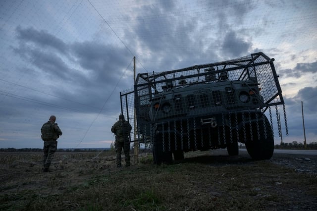 Des soldats ukrainiens devant un véhicule militaire blindé entouré d'une cage de protection contre les attaques de drones, sur une route près d'Oleksandrivka, le 6 octobre 2025