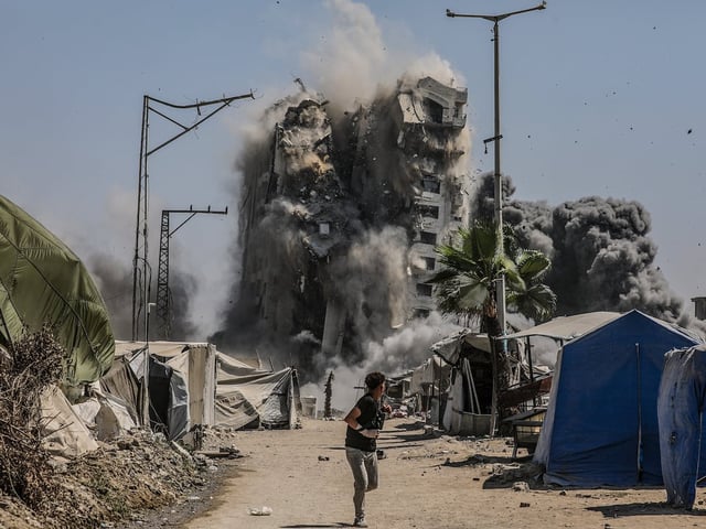Un adolescente palestino corre durante el colapso de una torre de viviendas en la Ciudad de Gaza, destruida por Israel la víspera del segundo aniversario del 7-O