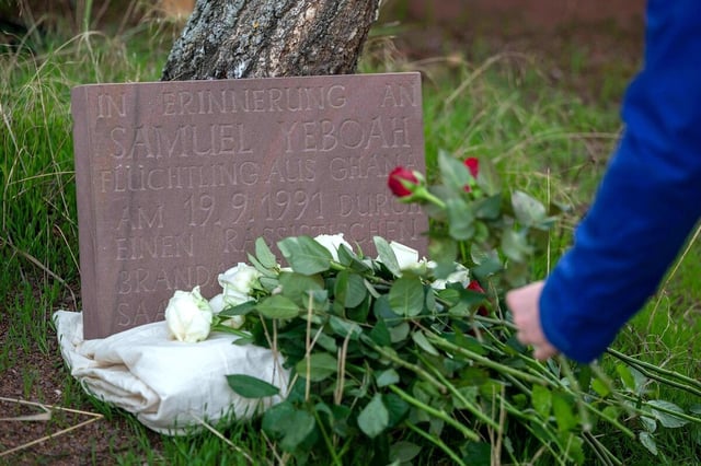 Ein gedenkstein, vor dem rote Rosen abgelegt werden