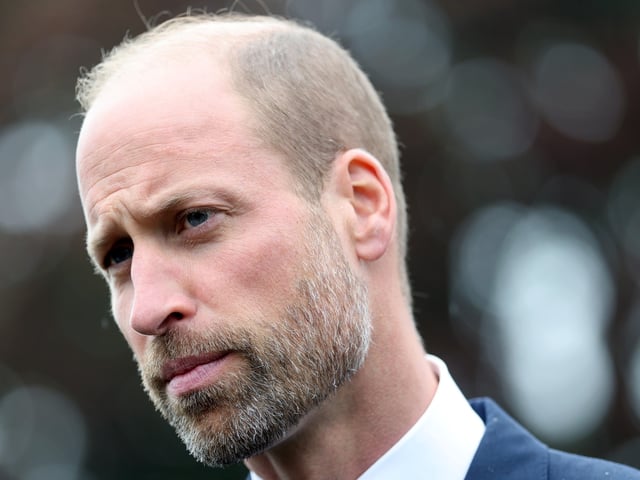 Prince William wearing a white shirt and blue jacket looking stern