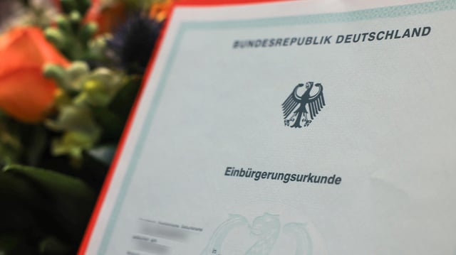 Eine Einbürgerungsurkunde wird vor einem Blumenstrauß gehalten.
