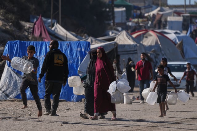 Palestinians carry plastic bottles to collect water in an area of a makeshift tent camp for displaced people along the shore of Nuseirat, in the central Gaza Strip, Wednesday, Oct. 8, 2025. (AP Photo/Abdel Kareem Hana)