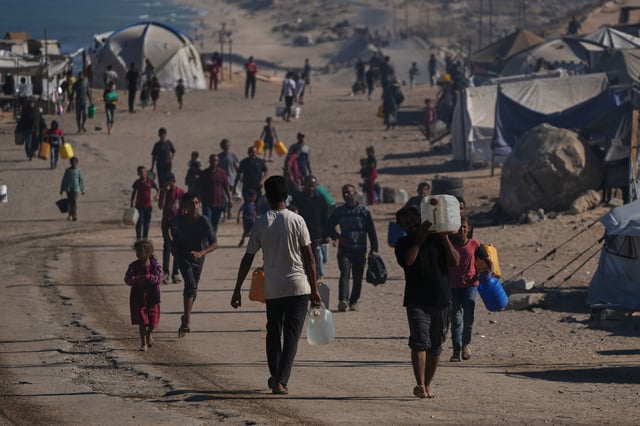 Palestinians carry plastic bottles with water in an area of a makeshift tent camp for displaced people along the shore of Nuseirat, in the central Gaza Strip, Wednesday, Oct. 8, 2025. (AP Photo/Abdel Kareem Hana)