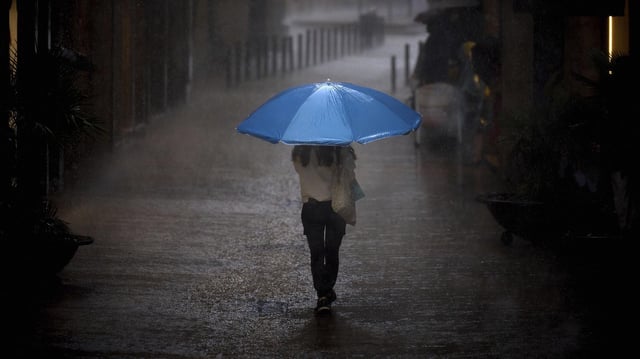 Eine Frau spaziert mit einem Regenschirm durch den Regen.