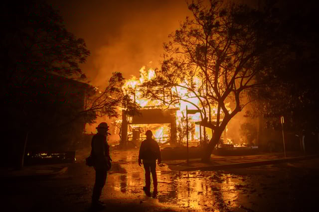 Firefighters watch the flames from the Palisades Fire burning a home on January 8, in the Pacific Palisades neighborhood of Los Angeles, California.