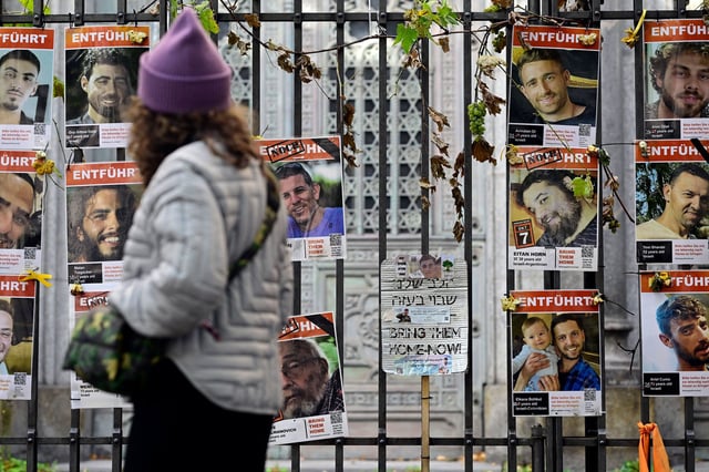A woman passes a placard with the lettering 'Bring them home now' that is seen among portraits of hostages and victims of Palestinian militant group Hamas that are attached to the fence of the New Synagogue in Berlin on October 6, 2025, one day before the second anniversary of Hamas's October 7, 2023 attack on Israel. Delegations from Hamas, Israel and the United States are due to convene in Egypt for talks on October 6, with US President Trump urging negotiators to "move fast" to end the nearly two-year war in Gaza. Both Hamas and Israel have responded positively to Trump's proposal for an end to the fighting and the release of captives in Gaza in exchange for Palestinians held in Israeli jails. (Photo by John MACDOUGALL / AFP) (Photo by JOHN MACDOUGALL/AFP via Getty Images)          