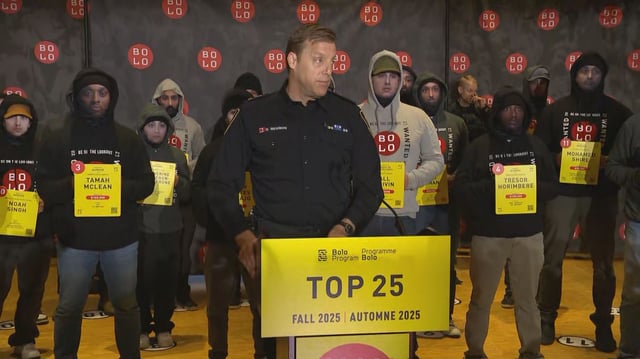Vancouver Police supt. Dale Weidman speaks at a press conference as 25 police officers wearing face masks of Canada's 25 most wanted fugitives stand behind him on Oct. 8, 2025.