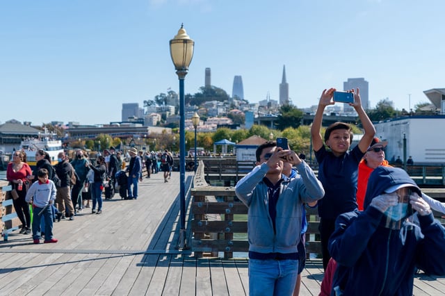 A family tries to capture the action of the United Airlines Boeing 777 plane flying by Pier 41 in San Francisco, on Oct. 8, 2022