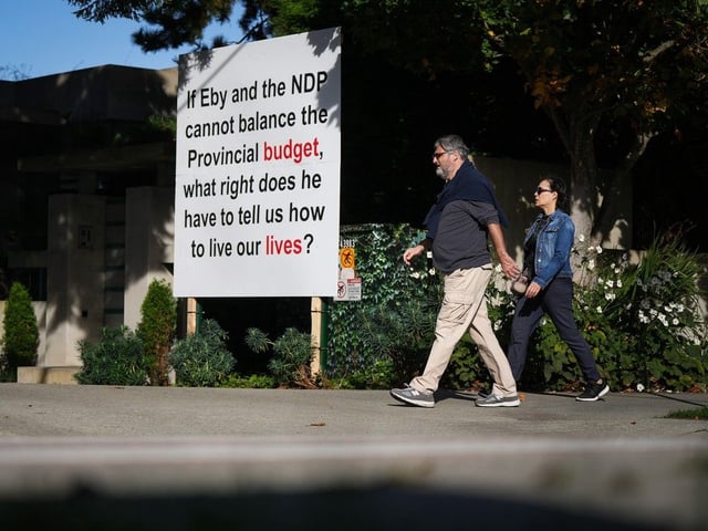  Pedestrians walk past another provincial election-related sign outside the home of billionaire Lululemon founder Chip Wilson in Vancouver on Oct. 10, 2024.