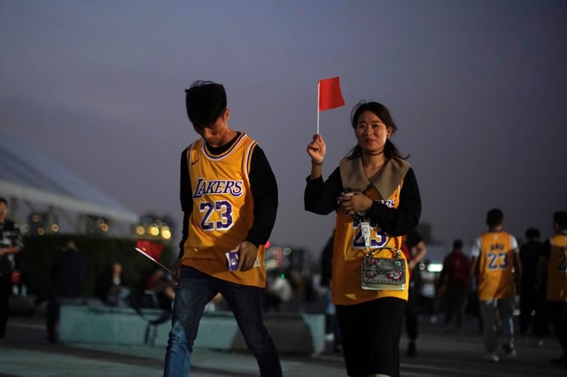 A woman and a man in LeBron James jerseys hold Chinese national flags as they walk into the Mercedes-Benz Arena before the NBA exhibition game between Brooklyn Nets and Los Angeles Lakers in Shanghai, China, on October 10, 2019.
