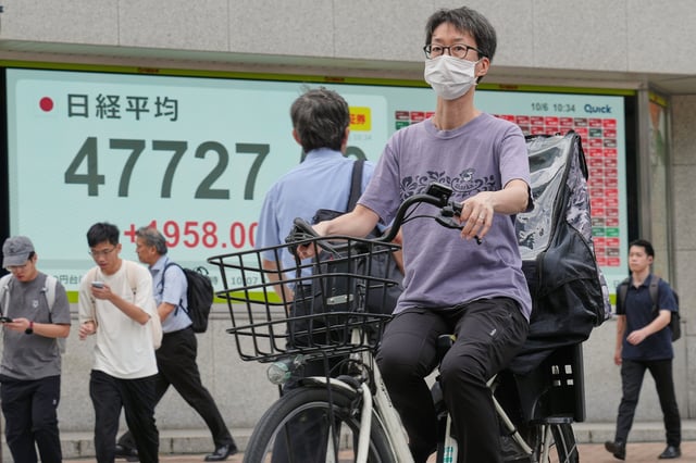 A person rides a bicycle in front of an electronic stock board showing Japan's Nikkei index at a securities firm Monday, Oct. 6, 2025, in Tokyo. (AP Photo/Eugene Hoshiko)